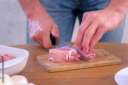 Man cutting fresh fillet meat pork on pieces to cook shashlik, hands closeup. He cutting on wooden board kitchen table. Prepare cook food for grilling on grill. Spices, butter and onions on table.