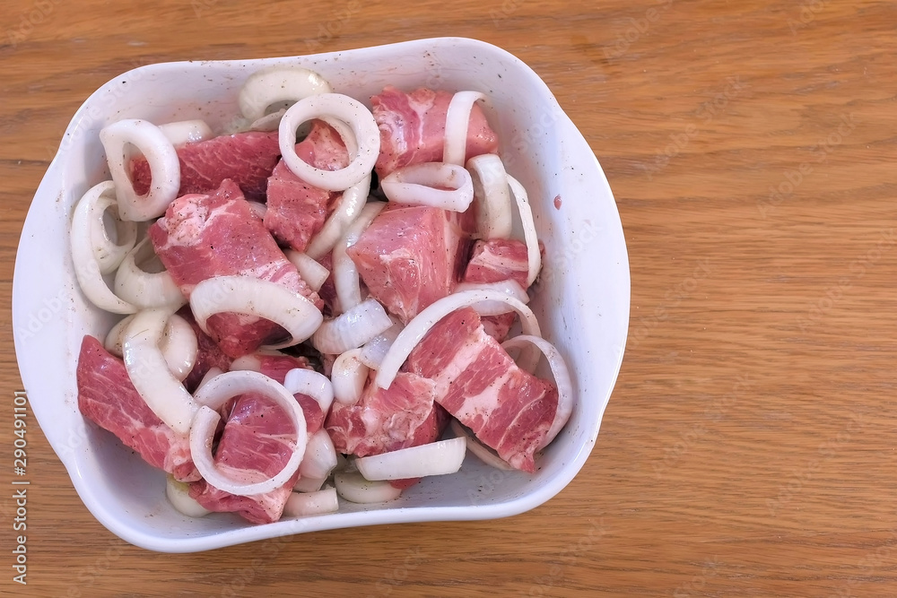 Pieces of raw fillet pork meat with onion and spices marinating for shashlik, closeup top view. Prepare raw meat for barbeque and grilling witt salt, pepper and oil.
