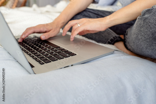 Happy woman with laptop in bed. Girl freelancer works in the home. Female in casual clothes. Online business. Remote job. Modern lifestyle, business day. Workspace. Mobile device. Typing on keyboard