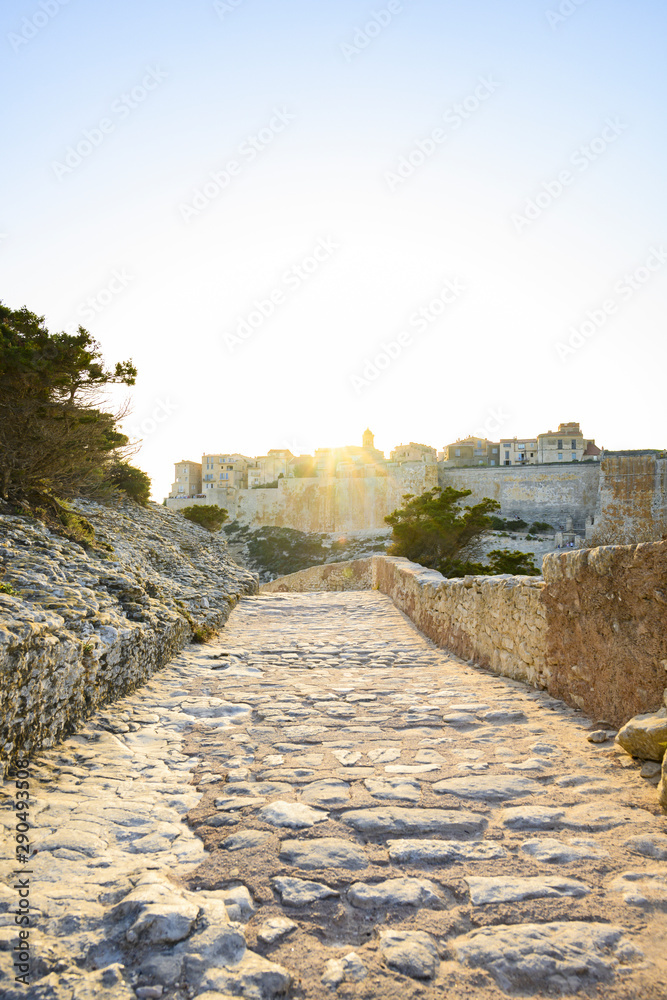 Stunning sunset that illuminates a pathway that leads to the beautiful village of Bonifacio surrounded by ancient walls. South of Corsica, France.