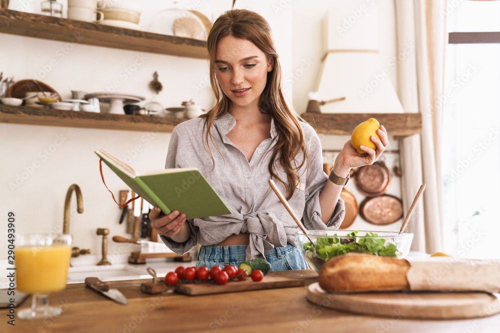 Woman indoors at the kitchen cooking holding notebook and lemon.