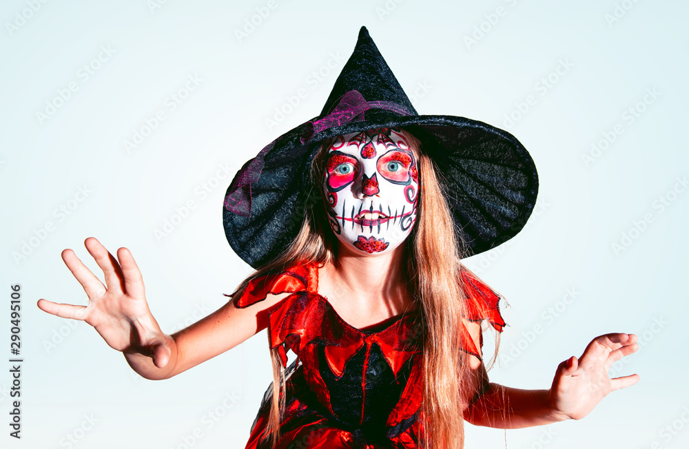 Little girl like a witch in scary red-black costume with glitter on white  background. Caucasian female model looks scary. Halloween, black friday,  sales, autumn holidays concept. The night of fear. Stock Photo