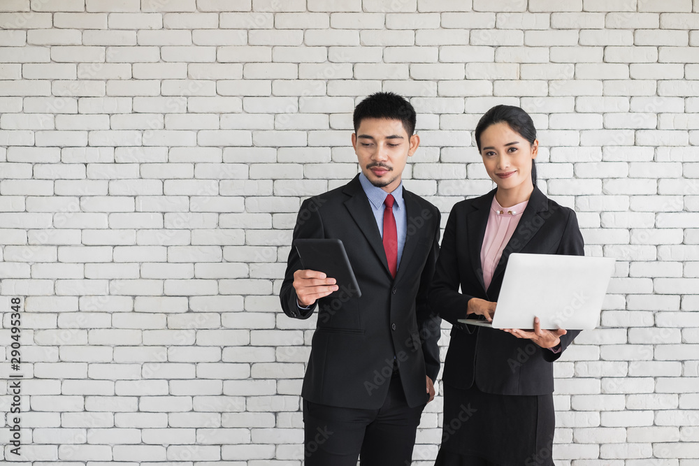Confidence young Asian business man looking at tablet and a woman in suit holding a laptop computer. Confidence young Asian business man looking at tablet and a woman in suit holding a laptop computer.