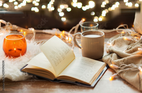 hygge and cozy home concept - book, cup of coffee or hot chocolate and candles with garland on window sill photo