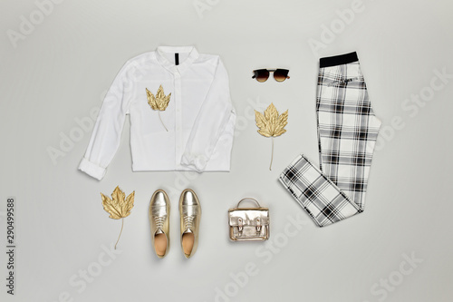 Fall fashion Flat lay. Trendy shirt, Stylish trousers, gold loafers shoes, glamour handbag, autumn maple leaf. Creative Woman Clothes Accessories Set, fall fashionable Outfit, autumnal color