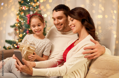 christmas, holidays and family concept - happy father, little daughter and mother with smartphone at home