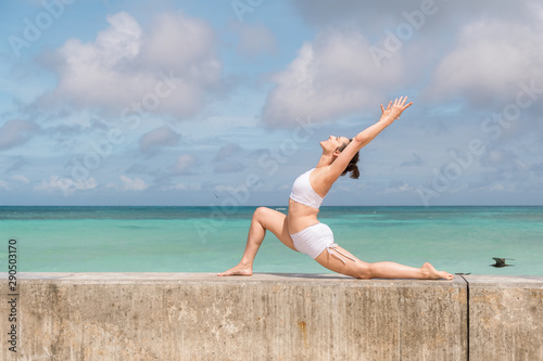Caucasian woman in white outfit practicing yoga at seaside