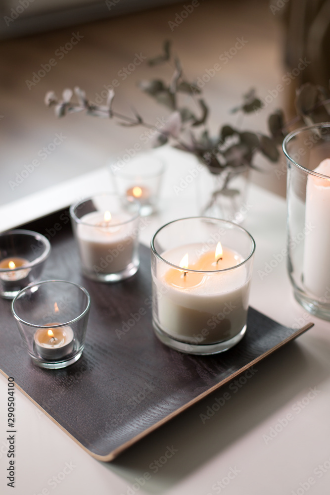 decoration, hygge and cosiness concept - burning white fragrance candles on tray on table at cozy home decoration, hygge and cosiness concept - burning white fragrance candles on tray on table at cozy home