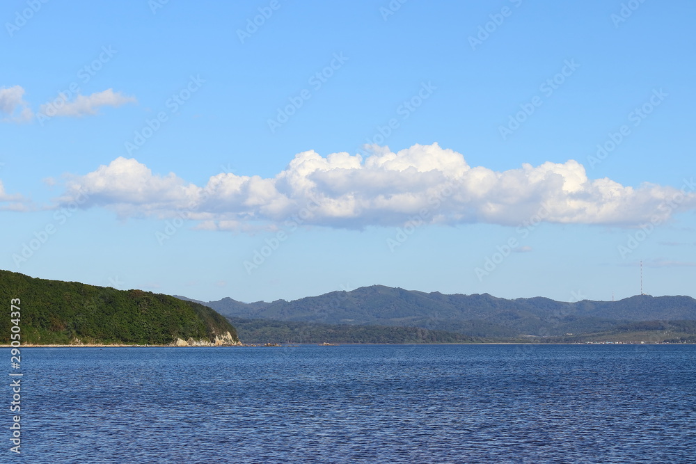 Green cape in blue sea under the clear blue sky with one wide cloud above.  Sunny day, calm blue water. Background, wallpaper , template.
