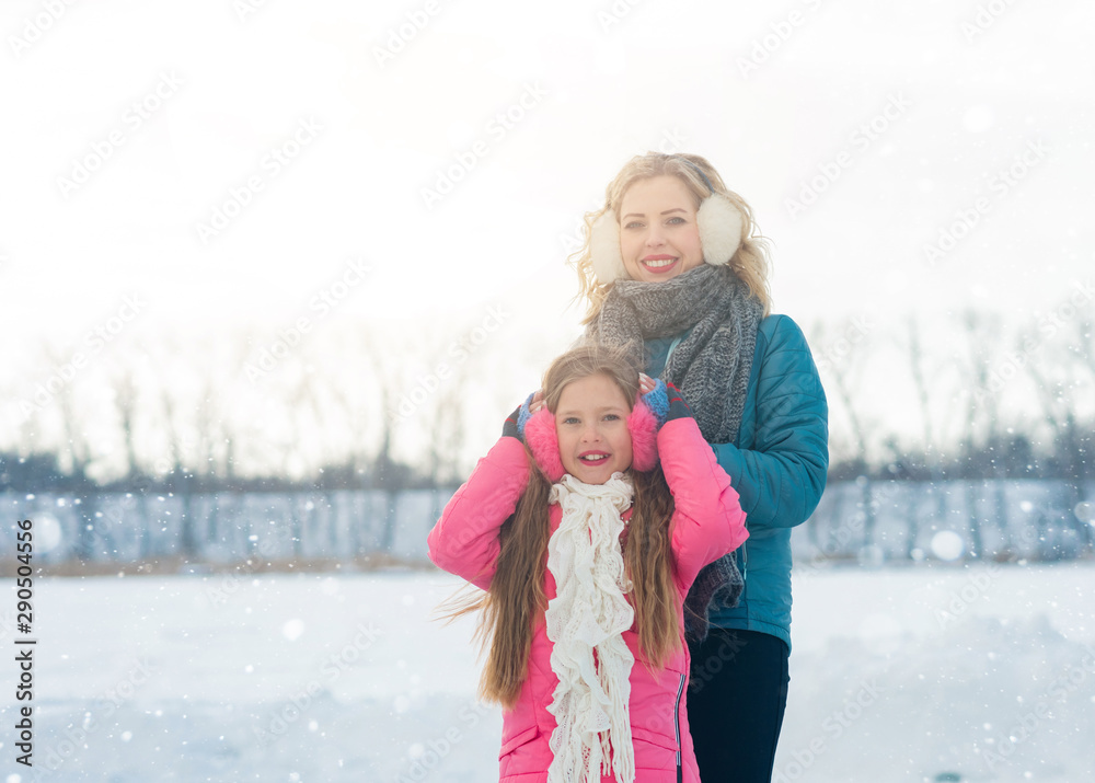 Obraz premium Smiling young mother and her cute daughter ice skating together by hands. Family skating and training with white skates on the ice area in winter day. Weekends activities outdoor in cold weather.