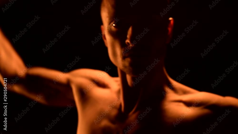 Close-up Slow motion of a young man in black pants in total darkness shows a representation of a rotating burning torch. Meditation in motion. Calm and unwavering. Work with fire. Low key Close-up Slow motion of a young man in black pants in total darkness shows a representation of a rotating burning torch. Meditation in motion. Calm and unwavering. Work with fire. Low key