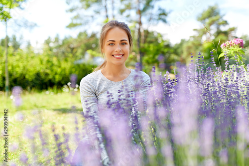 gardening and people concept - happy young woman sitting near lavender flowers on summer garden bed