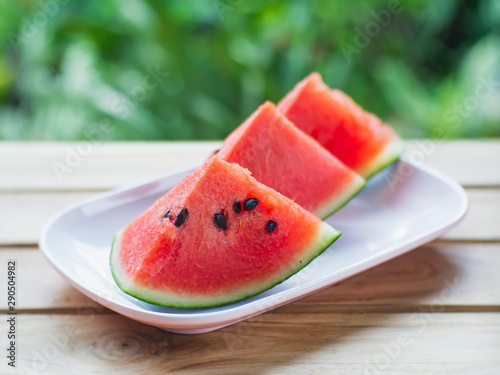 Watermelon sliced on a wooden table with green leaves in the background