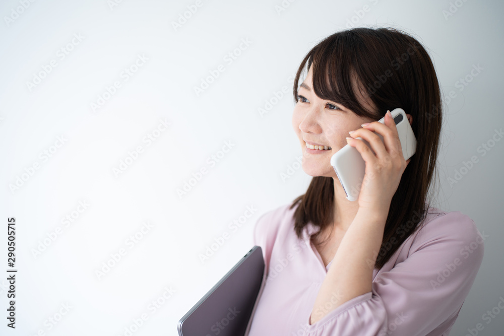 Young business woman holding smart phone and laptop computeragainst white wall Young business woman holding smart phone and laptop computeragainst white wall