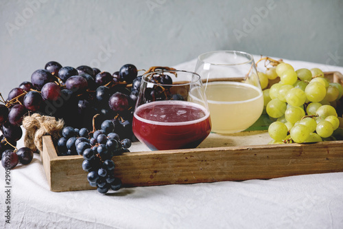 Traditional New european low alcohol red and white wine Federweisser or Neuer Wein, Burcak, Vin bourru in glasses with black and green grapes bunches in wooden tray on white table cloth. Copy space. photo