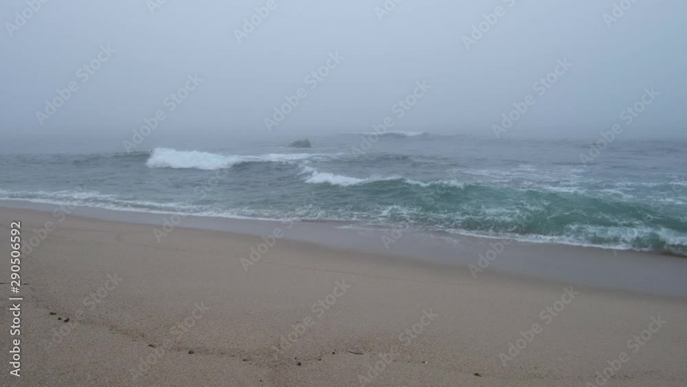 Slow motion waves breaking on a misty beach, with thick fog over the sea. Pan right.