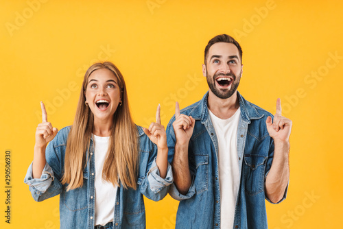 Fototapeta Image of surprised couple pointing fingers upward at copyspace