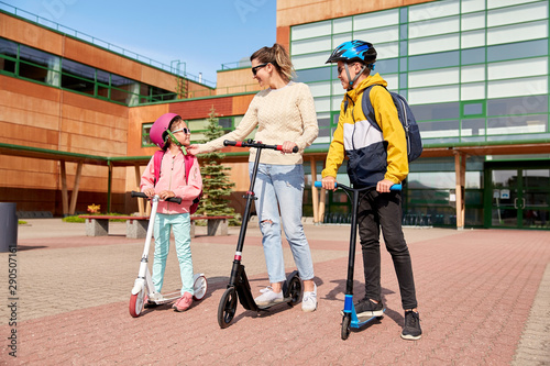 safety  school and family concept - happy daughter  son and mother riding scooters outdoors