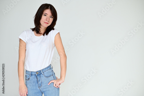 Portrait of a pretty asian brunette girl with black hair in a white t-shirt and blue jeans on a white background. It stands right in front of the camera, with emotions in various poses.