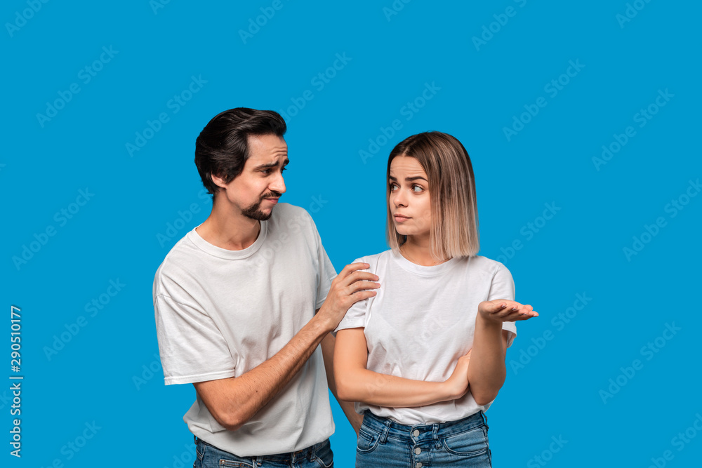 Brunet bearded man with mustaches in white t-shirt and blue jeans trying to cheer up his friend isolated over blue background. Concept of support. Brunet bearded man with mustaches in white t-shirt and blue jeans trying to cheer up his friend isolated over blue background. Concept of support.