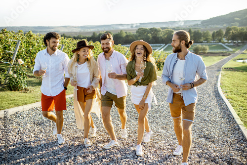 Canvas Print Group of young friends dressed casually hanging out together, walking with wine