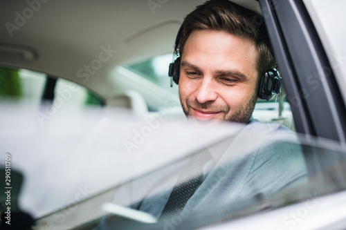 Young happy business man with headphones, shirt and tie sitting in car.
