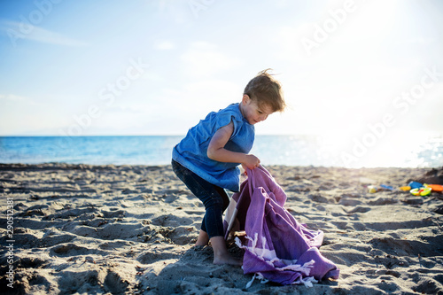 A portrait of small girl standing outdoors on sand beach, playing.