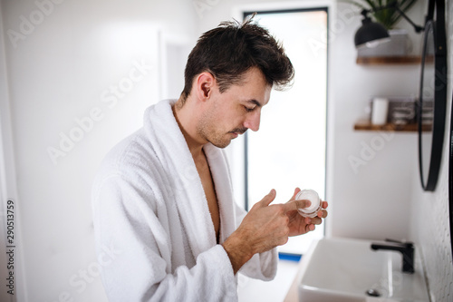 Young man putting cream on face in the bathroom in the morning, daily routine.