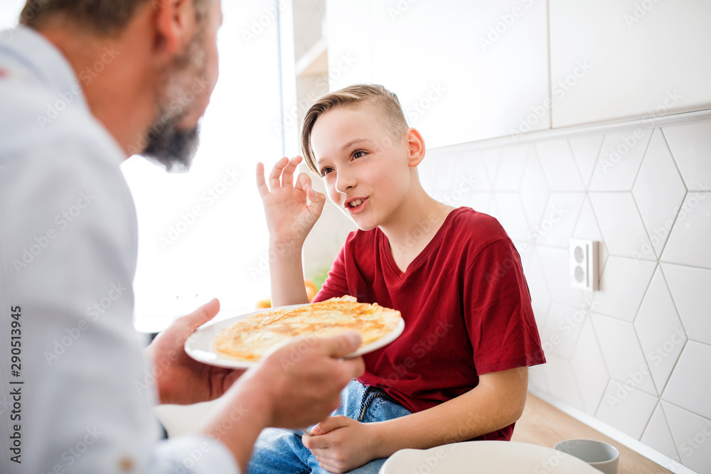 Mature father with small son indoors in kitchen, making pancakes.