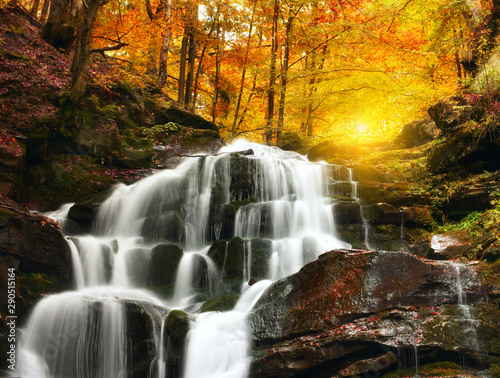 Waterfall Cascade in a beautiful deciduous autumn forest. Bright autumn leaves on stones covered with moss by the river. Beautiful autumn landscape. Long exposure.