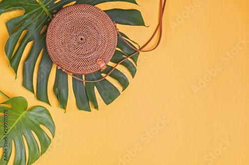 Trendy round eco bag from rattang lying on leaves of on big monstera plant photo