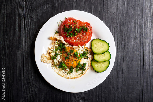 Grilled egg and grilled tomato on a plate on a wooden background. Fast and easy to prepare breakfast.