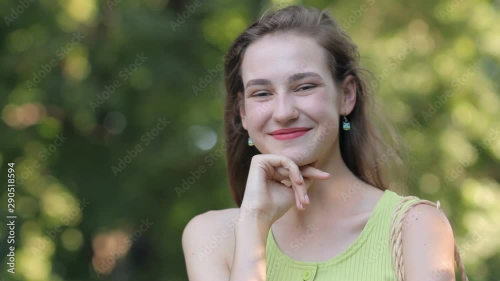 Young caucasian girl smiling portrait with hand under chin on green foliage background in summer day Young caucasian girl smiling portrait with hand under chin on green foliage background in summer day