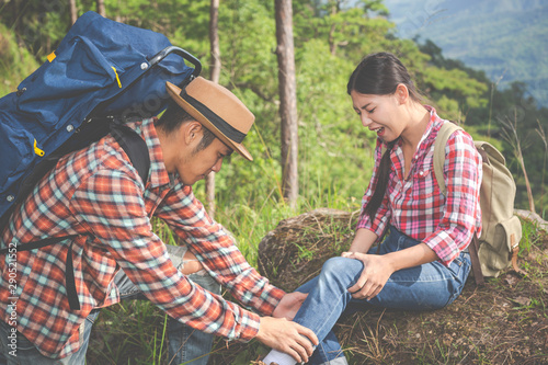 A young man massaging his girlfriend's legs, which pain in the top of the hill in a tropical forest, trekking adventure.