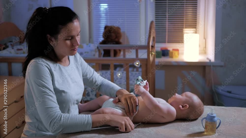Mom changes diaper baby at night. Beautiful caucasian girl mother changes diaper to her little child. Medium shot