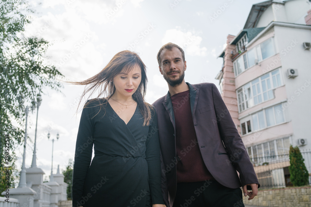 Happy pair. Walking In The City. Young couple walks holding woman in a long dress. Beautiful stylish pair of European looks A couple walks through the streets of the city. Happy pair. Walking In The City. Young couple walks holding woman in a long dress. Beautiful stylish pair of European looks A couple walks through the streets of the city.