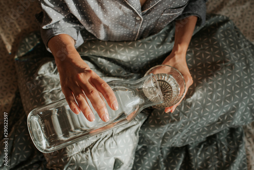 Woman in bed holding a glass of water in hand. Happy morning. Girl in pajamas. Healthy lifestyle, wellness. Proper nutrition. Drinking water. Morning with water. Sunlight on linens. Pillow, blanket