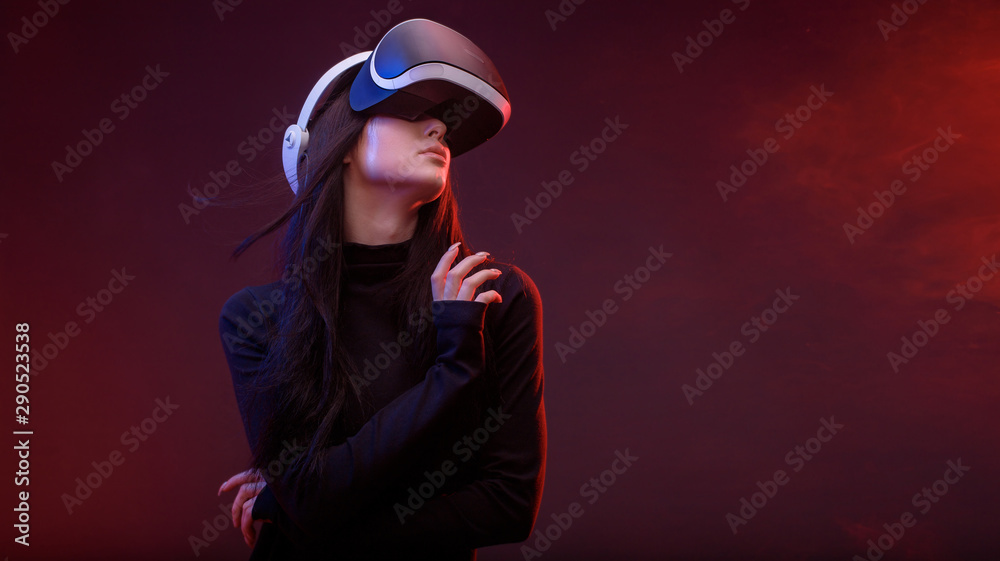 Beautiful woman with flowing hair in futuristic dress over dark background. Girl in glasses of virtual reality. Augmented reality, science, future technology, robots and people concept. VR. Beautiful woman with flowing hair in futuristic dress over dark background. Girl in glasses of virtual reality. Augmented reality, science, future technology, robots and people concept. VR.