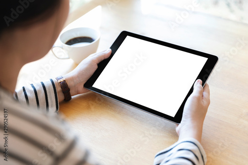 Hands holding black digital tablet pc with white blank screen on wooden table background in cafe.