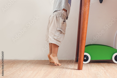 Closeup photo of Asian 18 months / 1 year old toddler baby boy child standing on tiptoes floor at home, Kid reaching up for things on the table - Soft & Selective focus