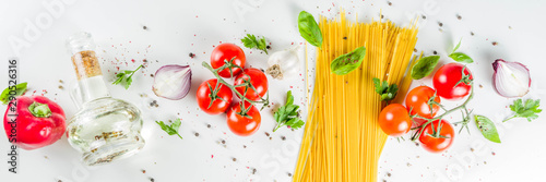 Traditional ingredients food spaghetti pasta. Mediterranean italian dinner concept background. Dried pasta, garlic, olive oil, basil, tomatoes. White stone background. Top view with copy space.