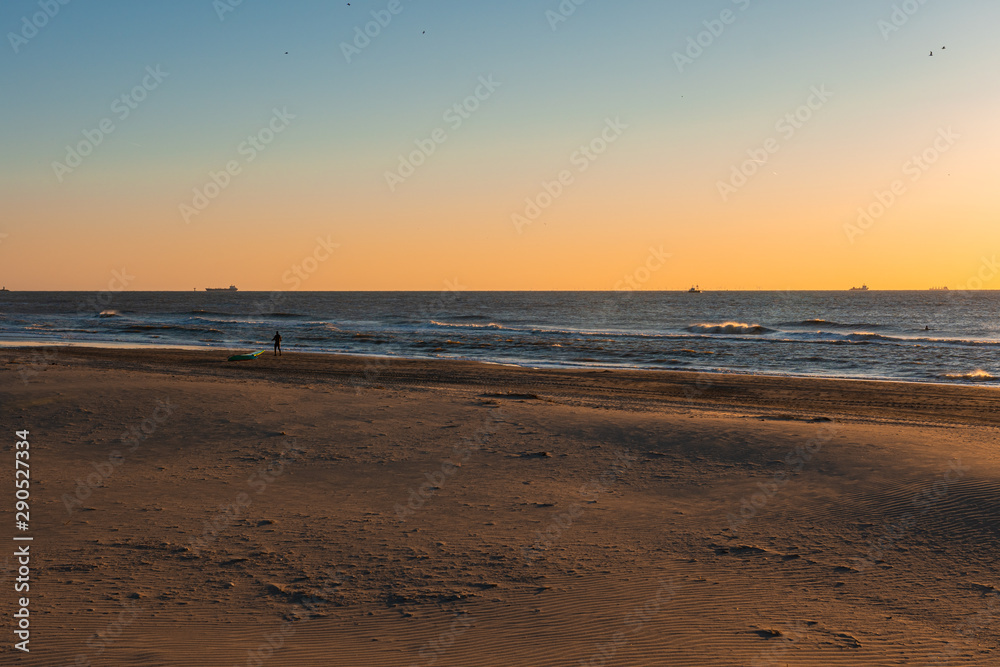 The sand beach fill the sunset light. The sea waves roll over. There is a ships on a horizon. the sand. The sand beach fill the sunset light. The sea waves roll over. There is a ships on a horizon. the sand.