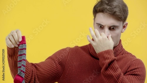 man in sweater smelling stinky sock isolated on yellow