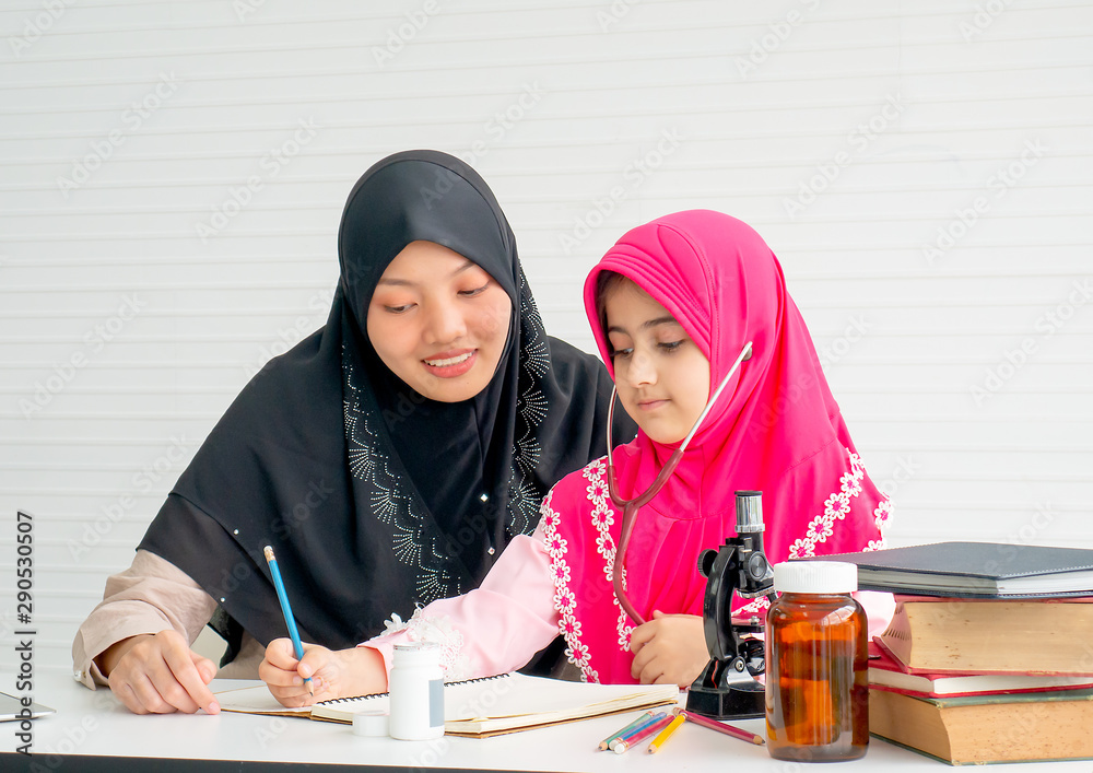 Muslim mother teach her daughter to learn about science and health in the room with white curtain. Muslim mother teach her daughter to learn about science and health in the room with white curtain.