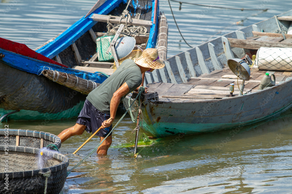 Man fishing with stick surrounded by colourful boats, Vietnam
