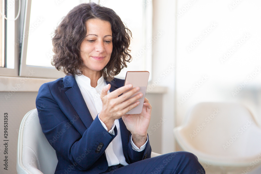 Satisfied customer using online mobile app. Business woman sitting in armchair, using mobile phone, looking at screen and smiling. Digital technology concept Satisfied customer using online mobile app. Business woman sitting in armchair, using mobile phone, looking at screen and smiling. Digital technology concept