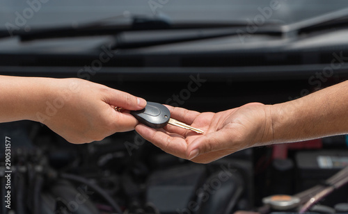 Close up of customer hand giving car key to car engine repairman on car engine background to repair it . Concept of maintenance vehicle mechanic and automotive