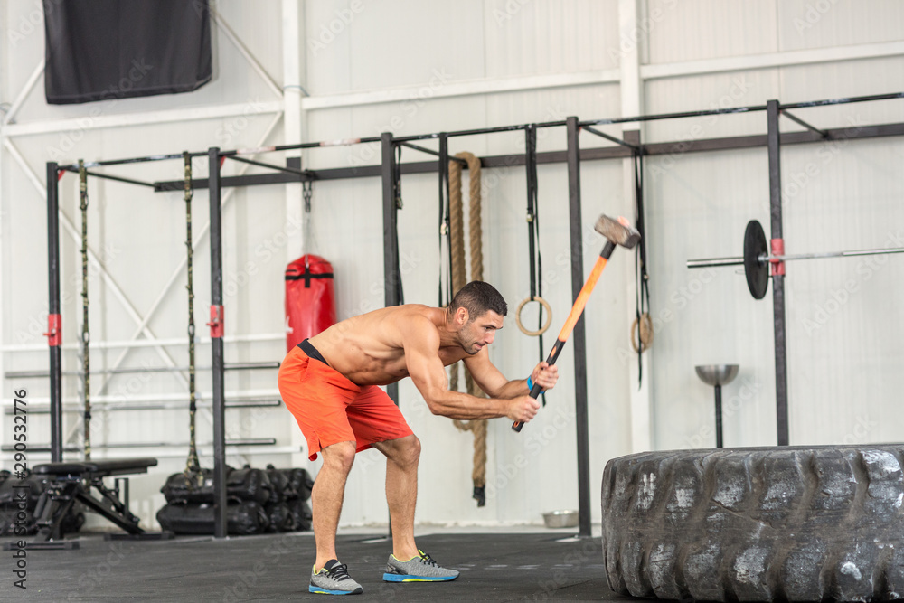 Fototapeta premium Sport fitness man hitting tractor tire with a sledgehammer