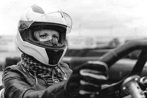 Portrait of a pretty girl wearing a white helmet close up, detail of Go-kart. karting track racing, copy space. serious look, determination, active lifestyle, black and white