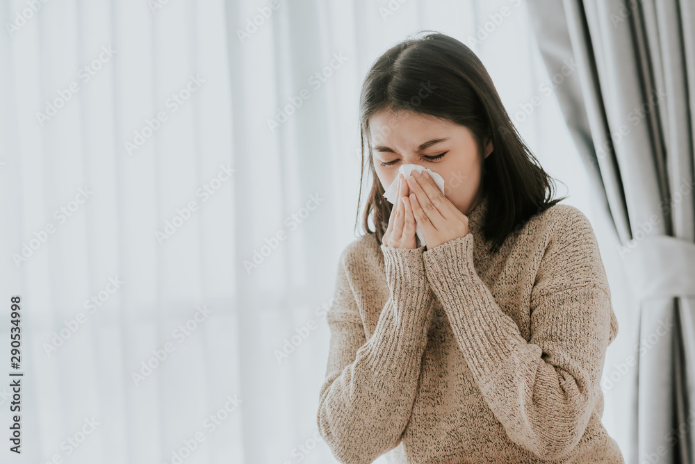 Sick Asian woman using a tissue to sneeze at home Sick Asian woman using a tissue to sneeze at home